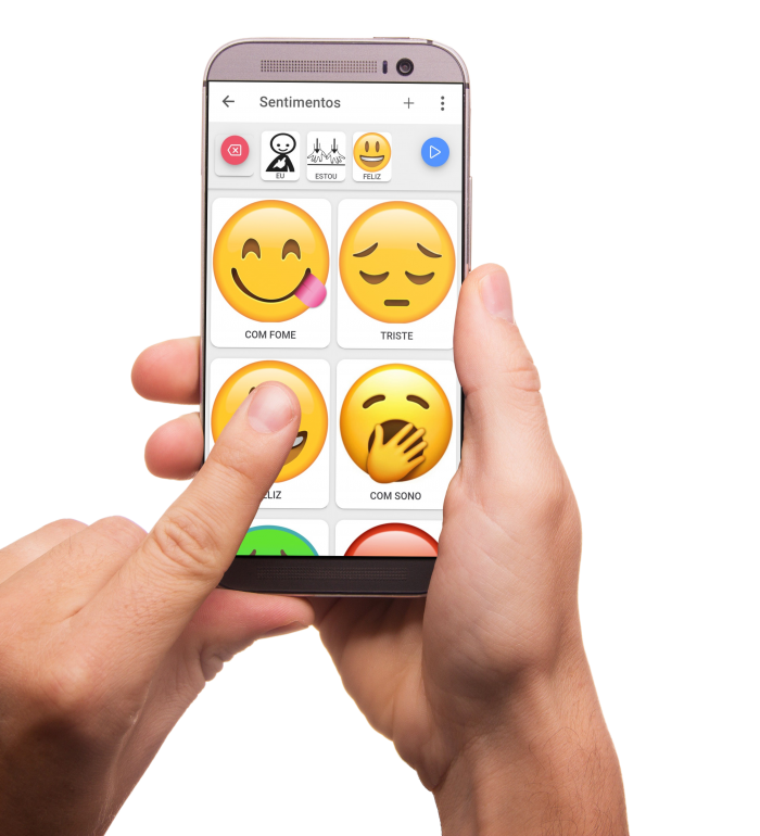 smartphone na mão direita, com o app Expressia mostrando diferentes emojis grandes na tela. Mão esquerda aponta o emoji Feliz enquanto a tela mostra a sequência de três imagens compondo a frase EU ESTOU FELIZ