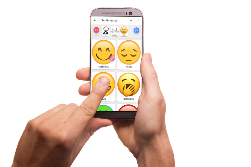 smartphone na mão direita, com o app Expressia mostrando diferentes emojis grandes na tela. Mão esquerda aponta o emoji Feliz enquanto a tela mostra a sequência de três imagens compondo a frase EU ESTOU FELIZ