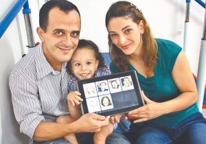 Casal com uma criança com paralisia cerebral sorriem com um tablet na mão rodando o app Livox