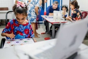 Menina com paralisia cerebral utilizando o teclado TiX para usar um notebook, que está a sua frente sobre uma mesa.