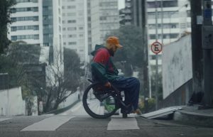 Homem em cadeira de rodas utilizando o tapete de acessibilidade Ford para poder subir da rua para ula calçada que não possui rampa.