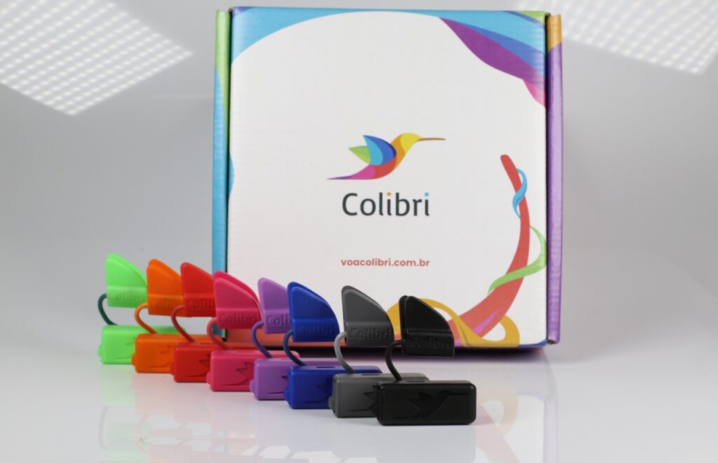 Oito aparelhos colibri, um de cada cor, enfileirados em frente à embalagem do produto