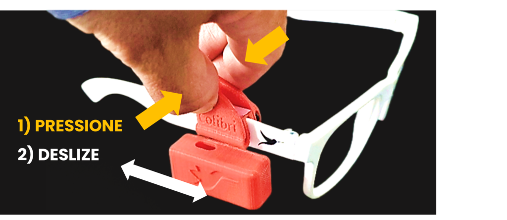 foto de dedos pressionando o prendedor do Colibri sobre a haste de um óculos, com setas indicando a direção para ajuste